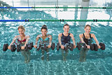 Smiling female fitness class doing aqua aerobics with foam dumbbells