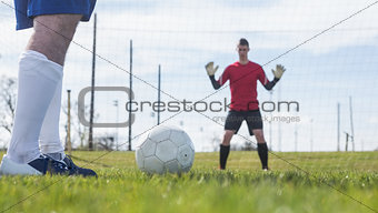 Goalkeeper in red waiting for striker to hit ball
