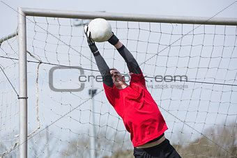 Goalkeeper in red jumping up to save a goal