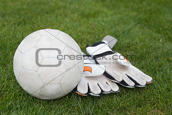 Goalkeeping gloves and football on pitch