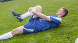 Football player in blue lying injured on the pitch