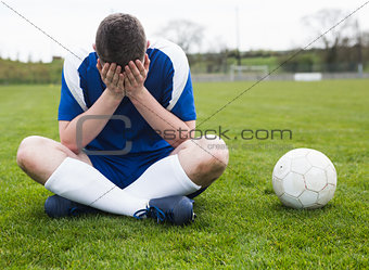 Disappointed football player in blue sitting on pitch after losing