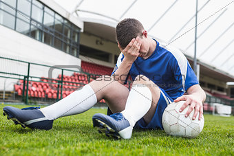 Disappointed football player in blue sitting on pitch after losing