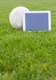 Football and tablet with blank screen on pitch