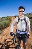 Fit cyclist smiling at the camera on country terrain