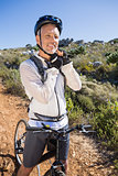 Fit cyclist adjusting helmet strap on country terrain smiling at camera