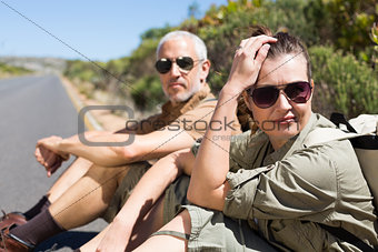 Hiking couple sitting on the side of the road looking at camera