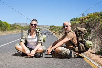 Hitch hiking couple sitting on the side of the road looking at camera