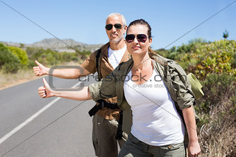 Hitch hiking couple standing on the side of the road with thumb out