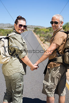 Hitch hiking couple holding hands on the road smiling at camera