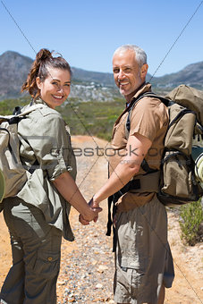 Happy hiking couple standing on mountain trail holding hands