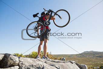 Fit man carrying his bike on rocky terrain