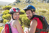 Fit cyclist couple sitting at the summit smiling at camera