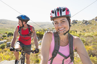 Fit cyclist couple smiling at camera on mountain trail