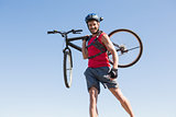 Fit cyclist carrying his bike on rocky terrain