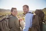 Hiking couple sitting on mountain terrain smiling at camera