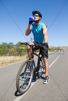 Handsome cyclist taking a break on his bike drinking water