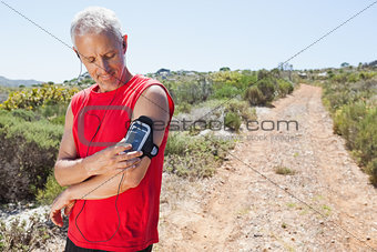 Fit man changing the song on his music player on mountain trail