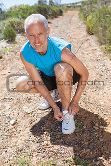 Smiling jogger tying his shoelace on mountain trail