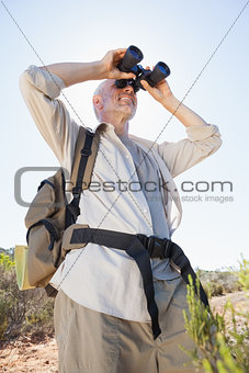 Hiker standing on country trail looking through binoculars