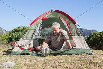 Happy camper cooking on camping stove outside his tent