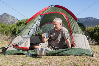 Happy camper holding mug outside his tent