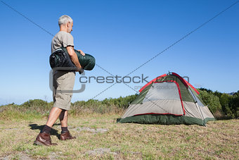 Happy camper walking towards his tent holding sleeping bag