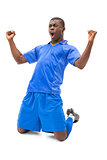 Excited football player in blue cheering on his knees