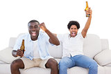Ecstatic sports fans sitting on the couch with beers