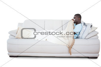 Sick man lying on couch blowing his nose