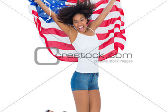 Pretty girl wrapped in american flag jumping and smiling at camera