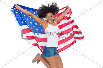 Pretty girl wrapped in american flag jumping and smiling at camera