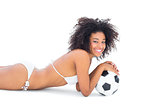 Fit girl in white bikini holding football lying on floor
