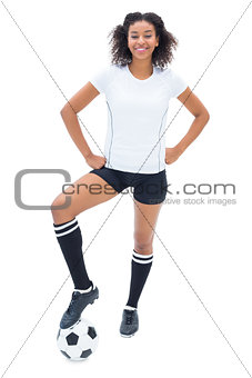 Pretty football player in white holding ball at her foot smiling at camera