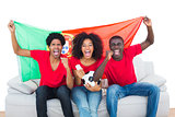 Cheering football fans in red sitting on couch with portugal flag