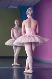 Graceful ballerina standing in first position in front of mirror
