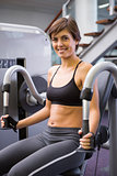 Smiling brunette using weights machine for arms