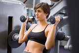 Smiling brunette using weights machine for arms