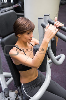 Focused brunette using weights machine for arms