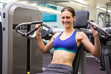 Fit smiling brunette using weights machine for arms