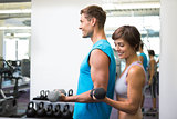 Fit happy couple lifting dumbbells together