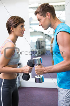 Fit couple lifting dumbbells together facing off