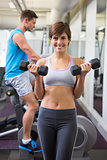 Fit brunette lifting weights smiling at camera