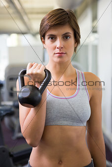 Fit brunette lifting kettlebell looking at camera