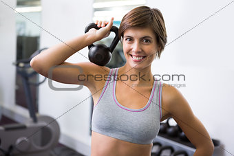 Fit brunette lifting kettlebell smiling at camera