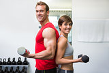 Fit couple lifting dumbbells together smiling at camera