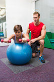 Personal trainer with client lifting dumbbells on exercise ball