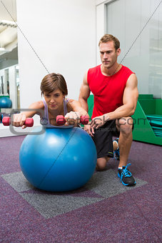 Personal trainer with client lifting dumbbells on exercise ball