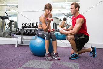 Personal trainer with client sitting on exercise ball lifting dumbbell