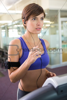 Fit brunette running on the treadmill listening to music